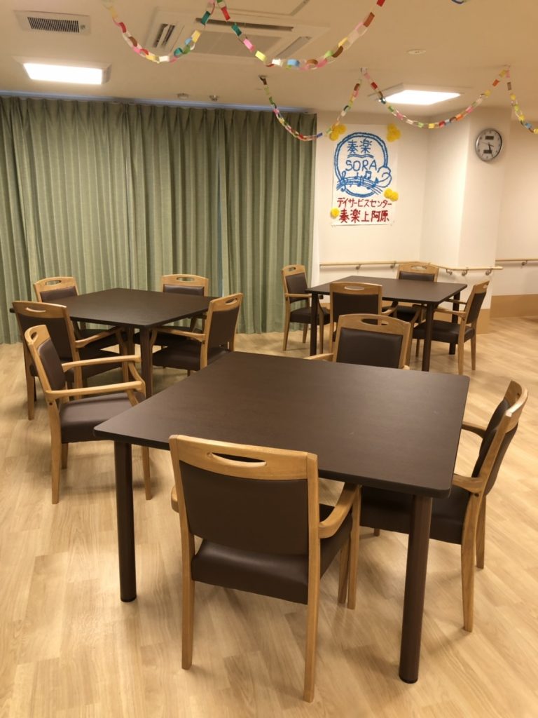 施設の共用スペース。複数のテーブルと椅子が配置され、クリスマス装飾で彩られた明るい居間